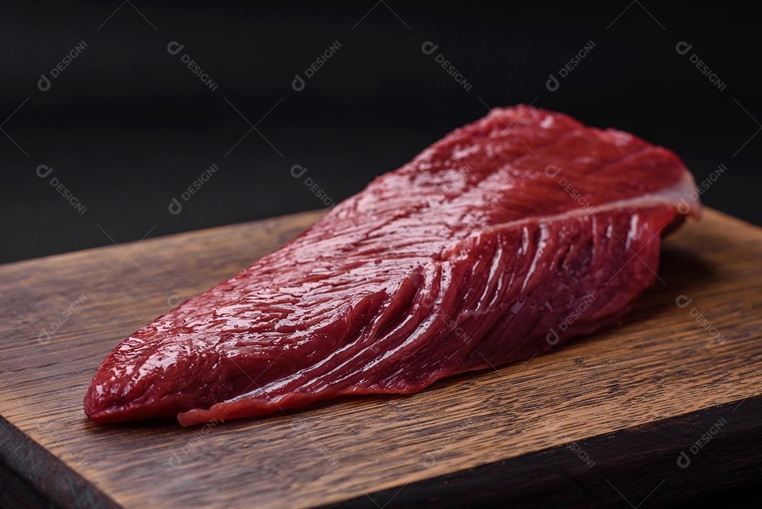 Belo pedaço fresco de carne crua em uma tábua de madeira sobre um fundo escuro de concreto