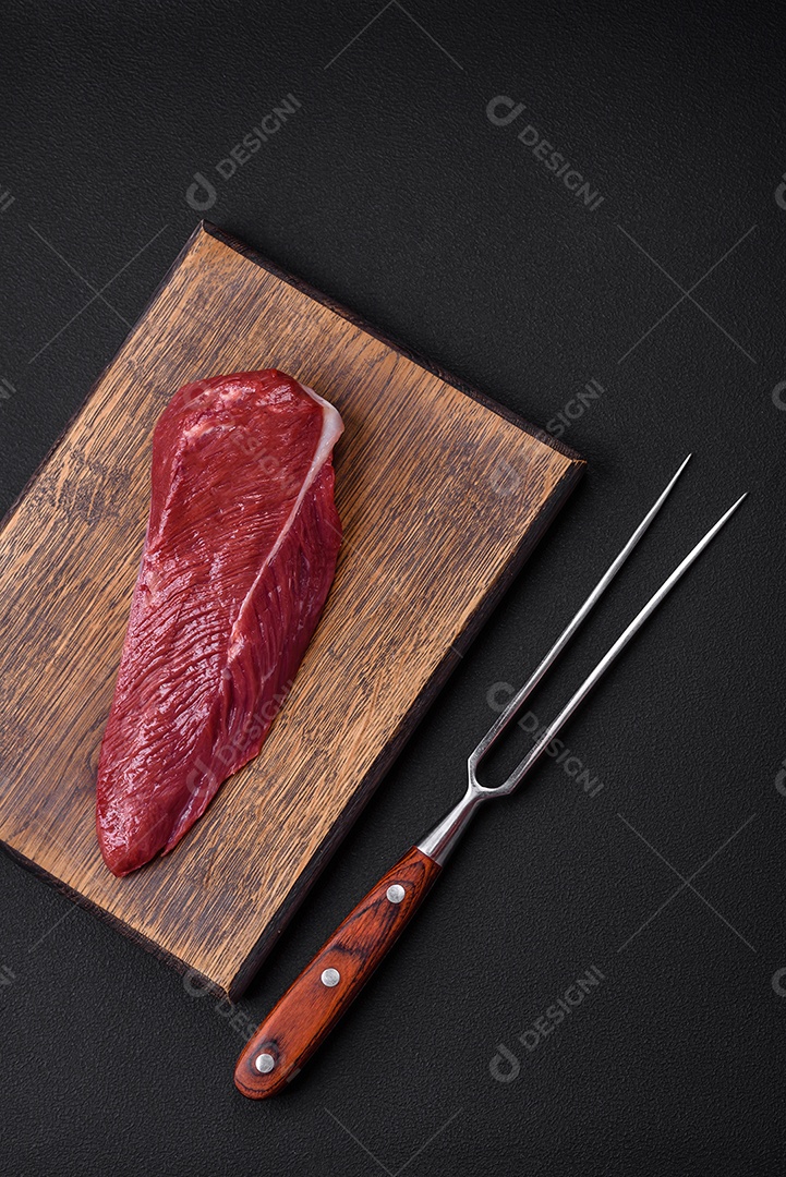Belo pedaço fresco de carne crua em uma tábua de madeira sobre um fundo escuro de concreto