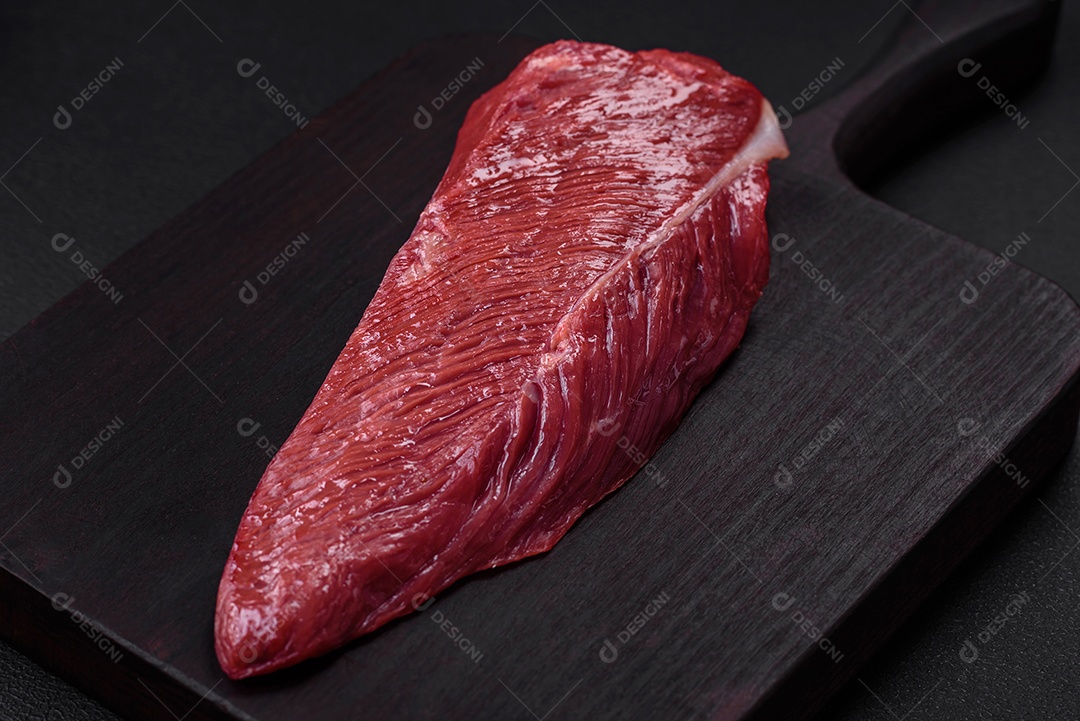 Belo pedaço fresco de carne crua em uma tábua de madeira sobre um fundo escuro de concreto