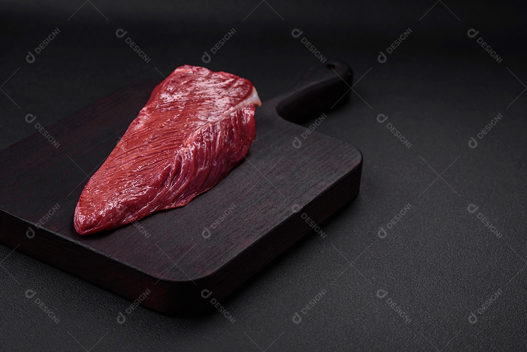 Belo pedaço fresco de carne crua em uma tábua de madeira sobre um fundo escuro de concreto