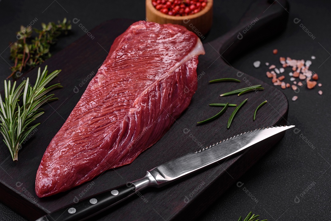 Belo pedaço fresco de carne crua em uma tábua de madeira sobre um fundo escuro de concreto