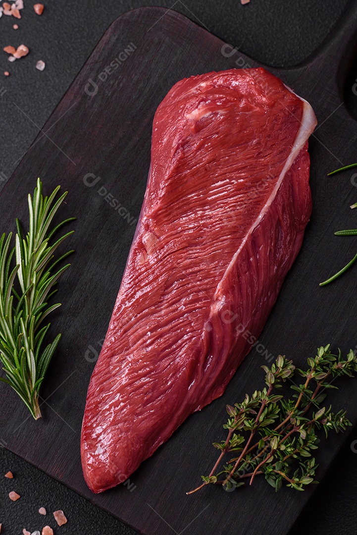 Belo pedaço fresco de carne crua em uma tábua de madeira sobre um fundo escuro de concreto