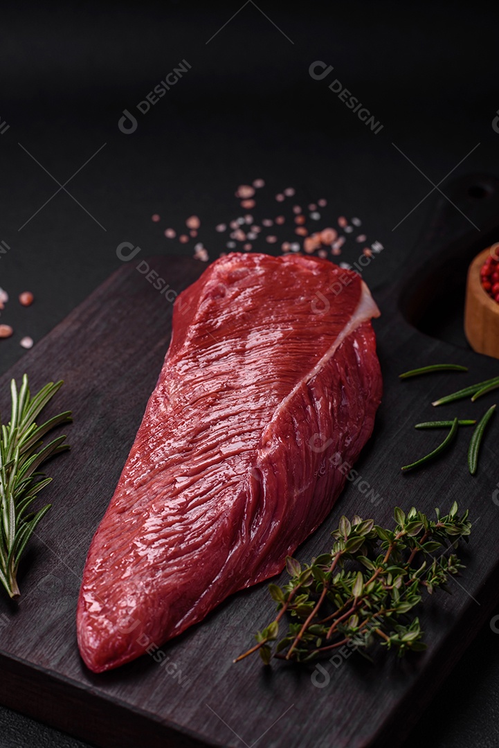 Belo pedaço fresco de carne crua em uma tábua de madeira sobre um fundo escuro de concreto