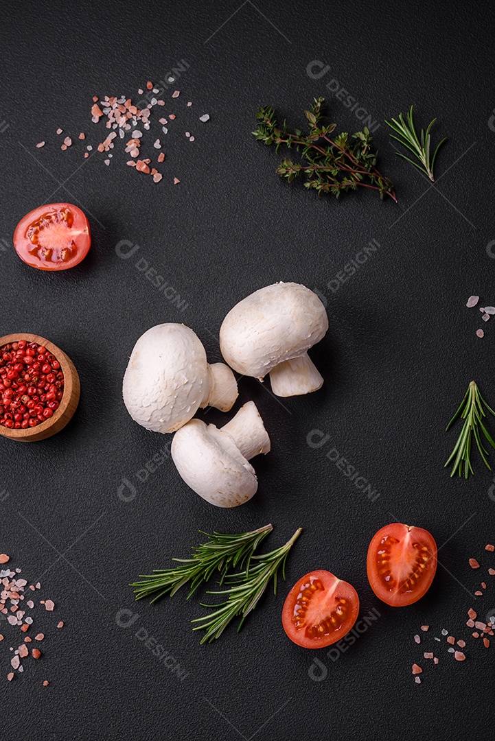 Cogumelos champignon crus frescos sobre uma tábua de madeira com especiarias e ervas sobre um fundo escuro de concreto