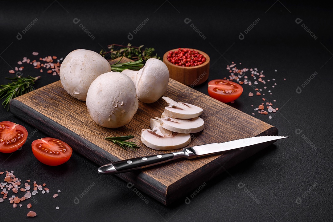 Cogumelos champignon crus frescos sobre uma tábua de madeira com especiarias e ervas sobre um fundo escuro de concreto