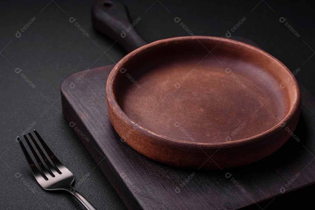 Placa cerâmica de cor marrom vazia em fundo de concreto texturizado escuro. utensílios de cozinha