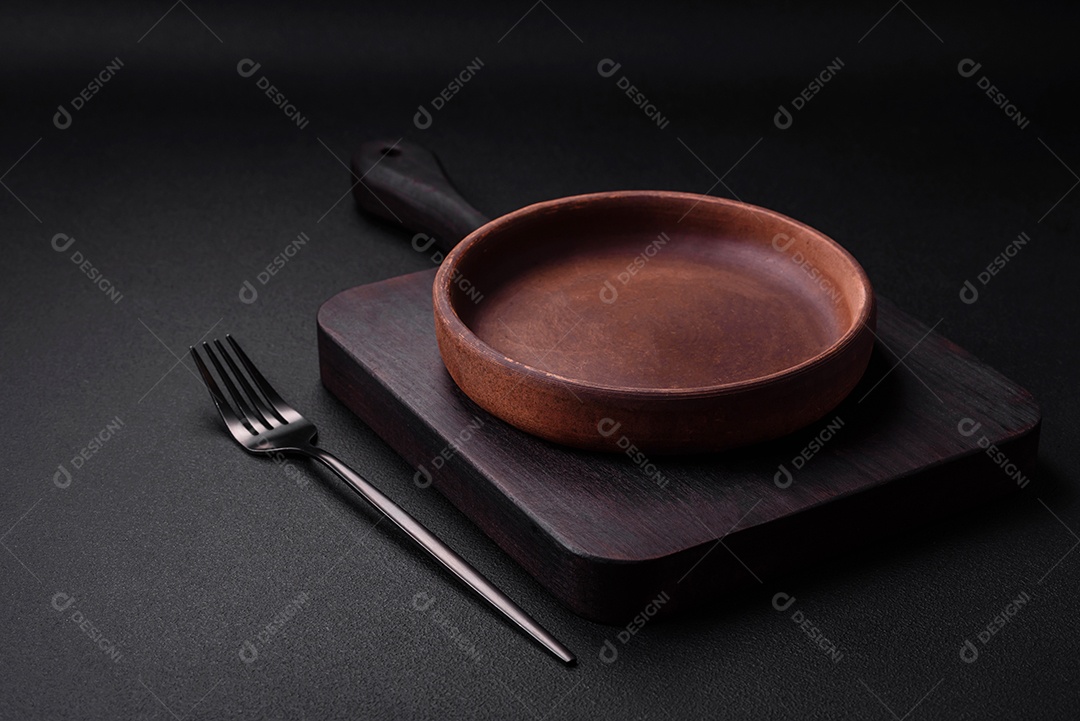 Placa cerâmica de cor marrom vazia em fundo de concreto texturizado escuro. utensílios de cozinha