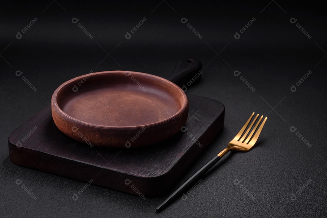 Placa cerâmica de cor marrom vazia em fundo de concreto texturizado escuro. utensílios de cozinha