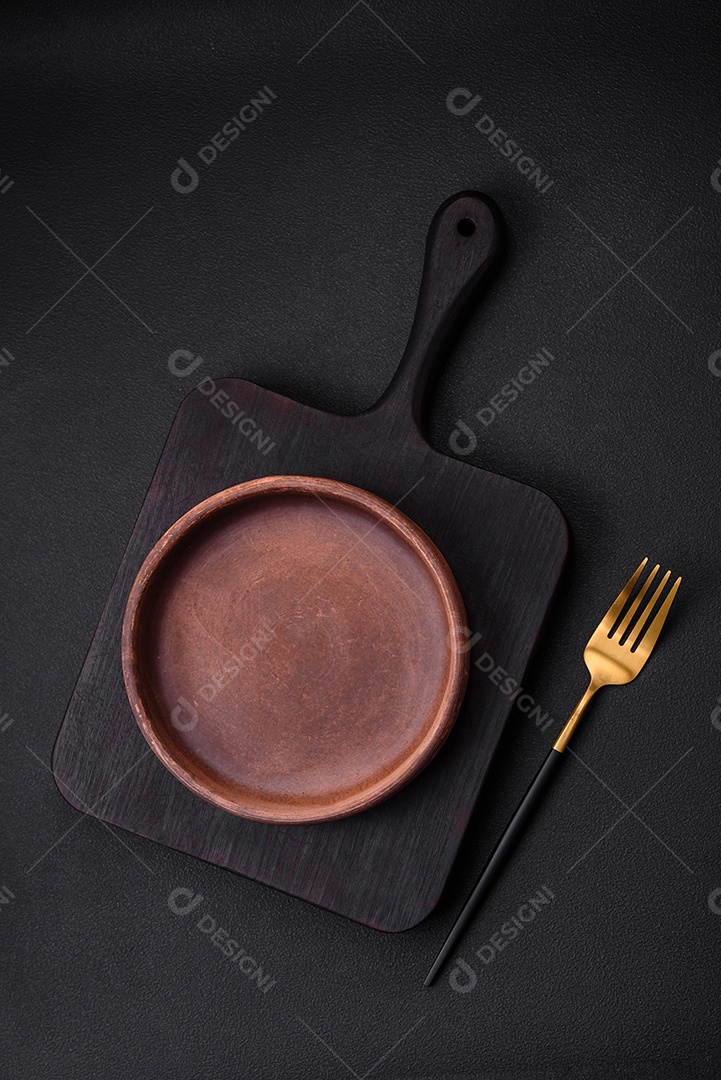 Placa cerâmica de cor marrom vazia em fundo de concreto texturizado escuro. utensílios de cozinha