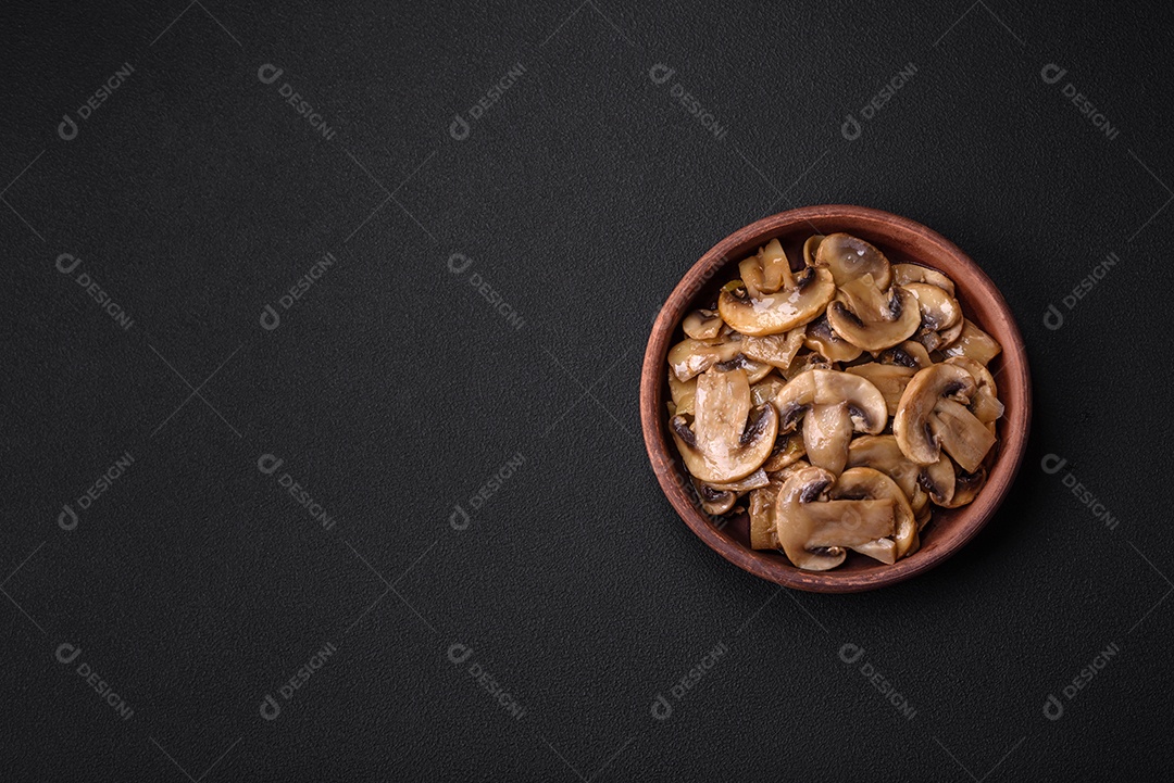 Cogumelos champignon fritos ou cozidos em forma de fatias com cebola num prato de cerâmica marrom sobre um fundo escuro de concreto