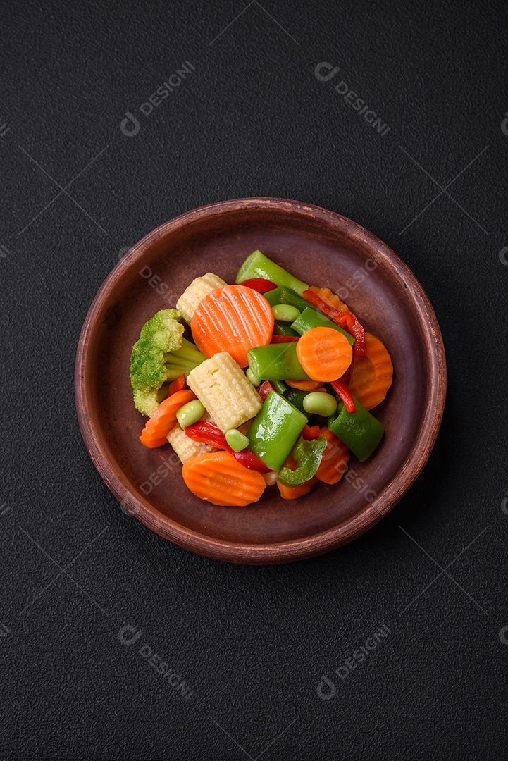 Deliciosos legumes saudáveis ​​cozidos cenouras, brócolis, feijão de espargos e pimentões em um fundo escuro de concreto