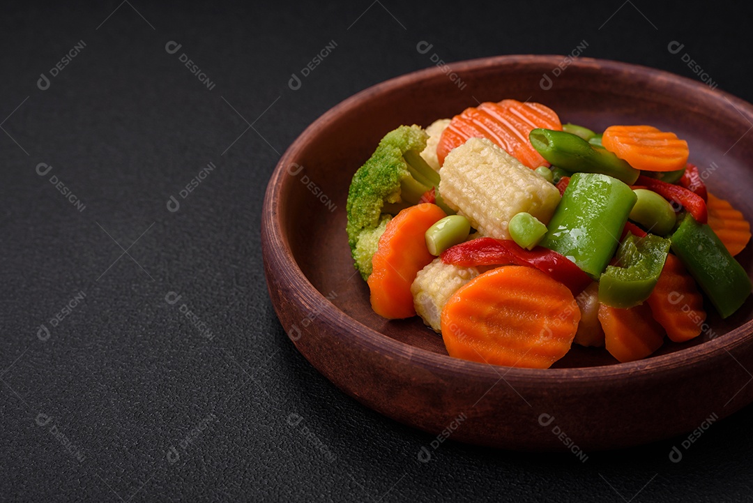 Deliciosos legumes saudáveis ​​cozidos cenouras, brócolis, feijão de espargos e pimentões em um fundo escuro de concreto