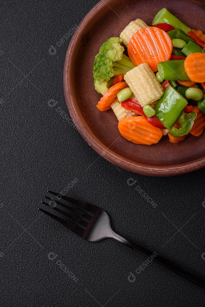 Deliciosos legumes saudáveis ​​cozidos cenouras, brócolis, feijão de espargos e pimentões em um fundo escuro de concreto