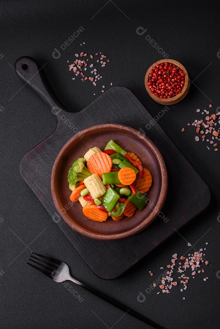 Deliciosos legumes saudáveis ​​cozidos cenouras, brócolis, feijão de espargos e pimentões em um fundo escuro de concreto