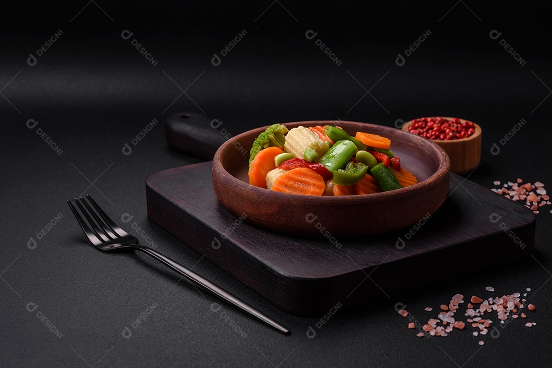 Deliciosos legumes saudáveis ​​cozidos cenouras, brócolis, feijão de espargos e pimentões em um fundo escuro de concreto