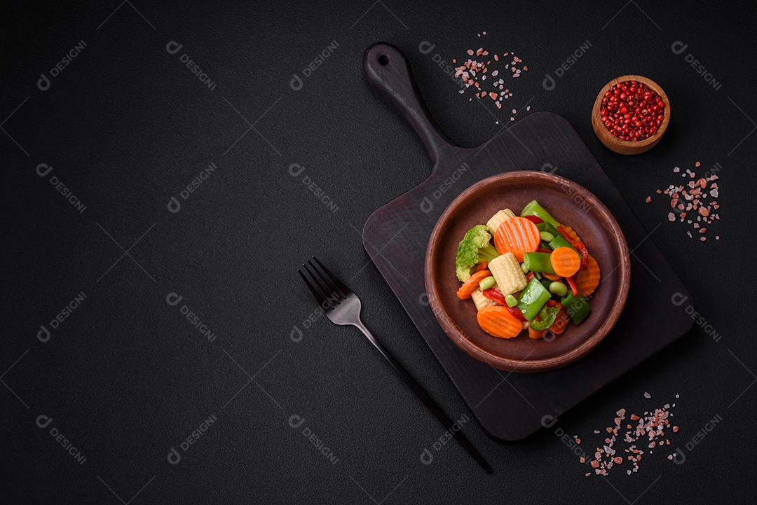 Deliciosos legumes saudáveis ​​cozidos cenouras, brócolis, feijão de espargos e pimentões em um fundo escuro de concreto