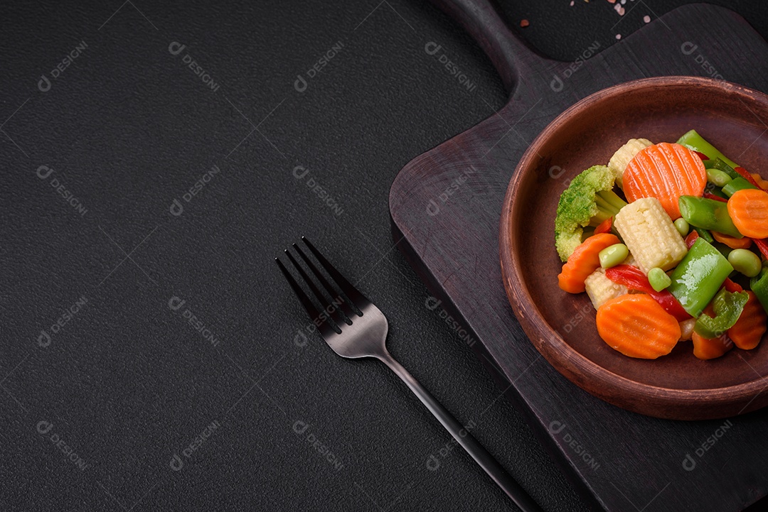 Deliciosos legumes saudáveis ​​cozidos cenouras, brócolis, feijão de espargos e pimentões em um fundo escuro de concreto