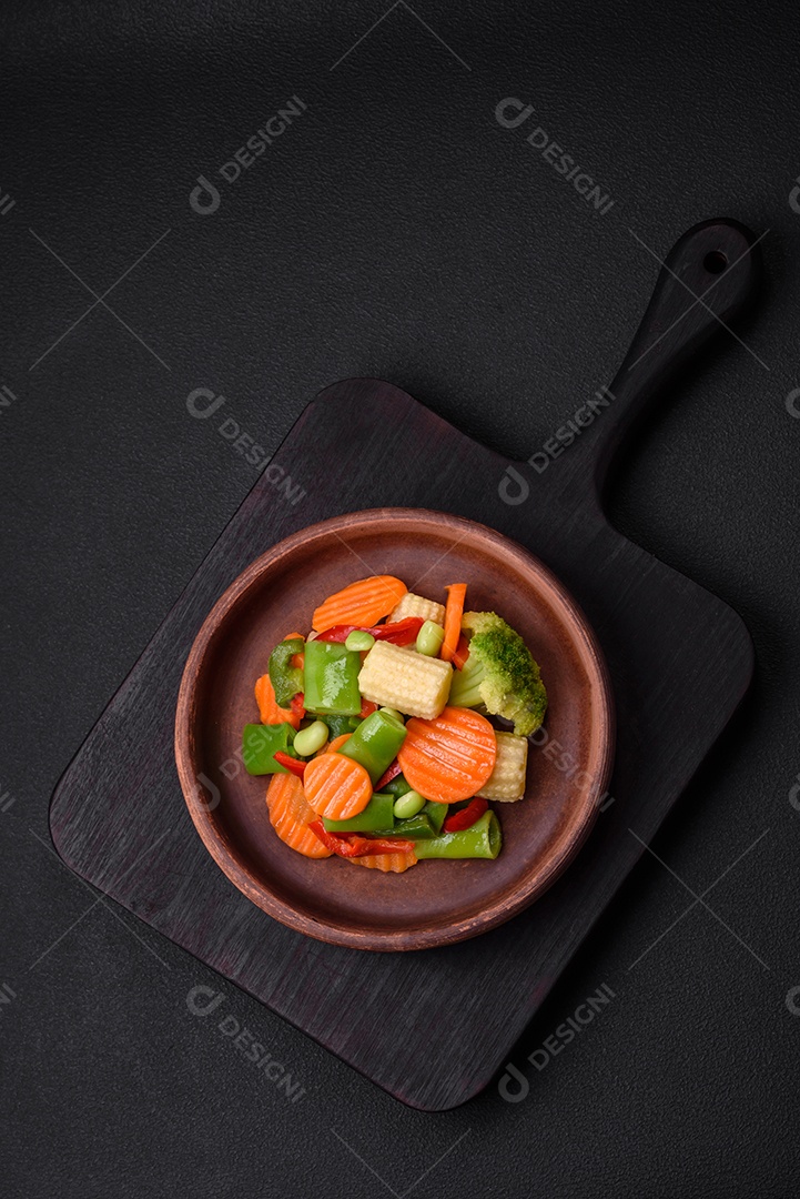 Deliciosos legumes saudáveis ​​cozidos cenouras, brócolis, feijão de espargos e pimentões em um fundo escuro de concreto