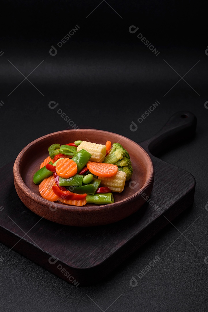 Deliciosos legumes saudáveis ​​cozidos cenouras, brócolis, feijão de espargos e pimentões em um fundo escuro de concreto