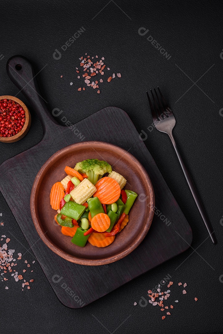 Deliciosos legumes saudáveis ​​cozidos cenouras, brócolis, feijão de espargos e pimentões em um fundo escuro de concreto