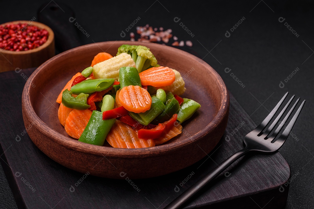 Deliciosos legumes saudáveis ​​cozidos cenouras, brócolis, feijão de espargos e pimentões em um fundo escuro de concreto