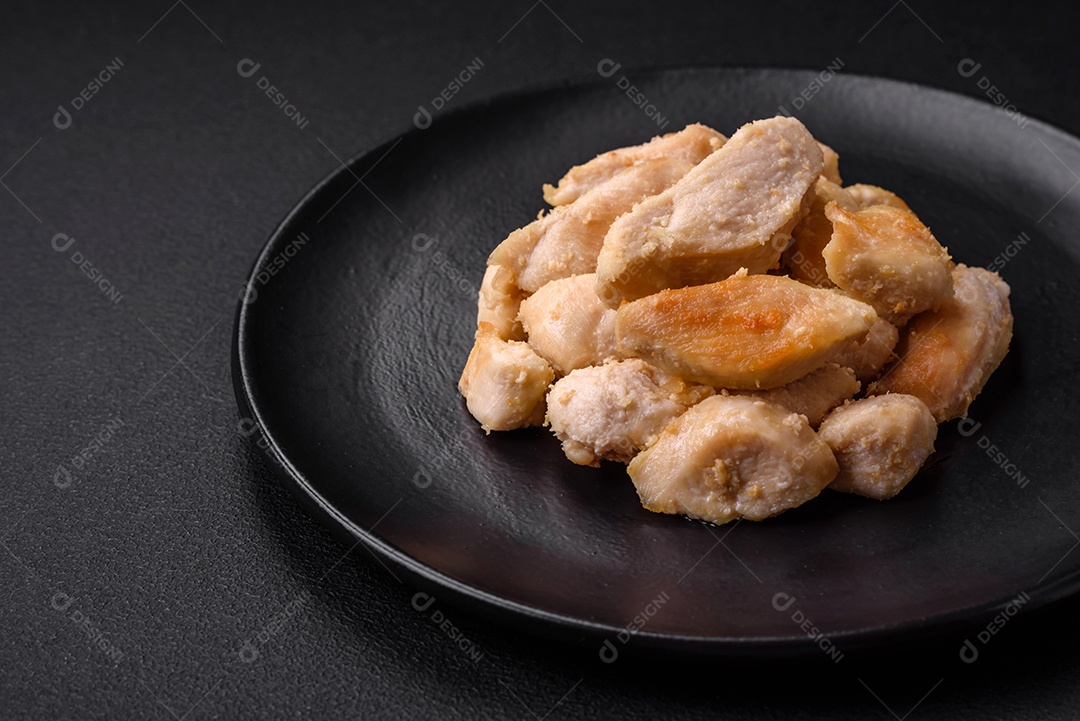 Deliciosas fatias de frango assadas com especiarias e ervas em uma placa cerâmica redonda sobre um fundo escuro de concreto