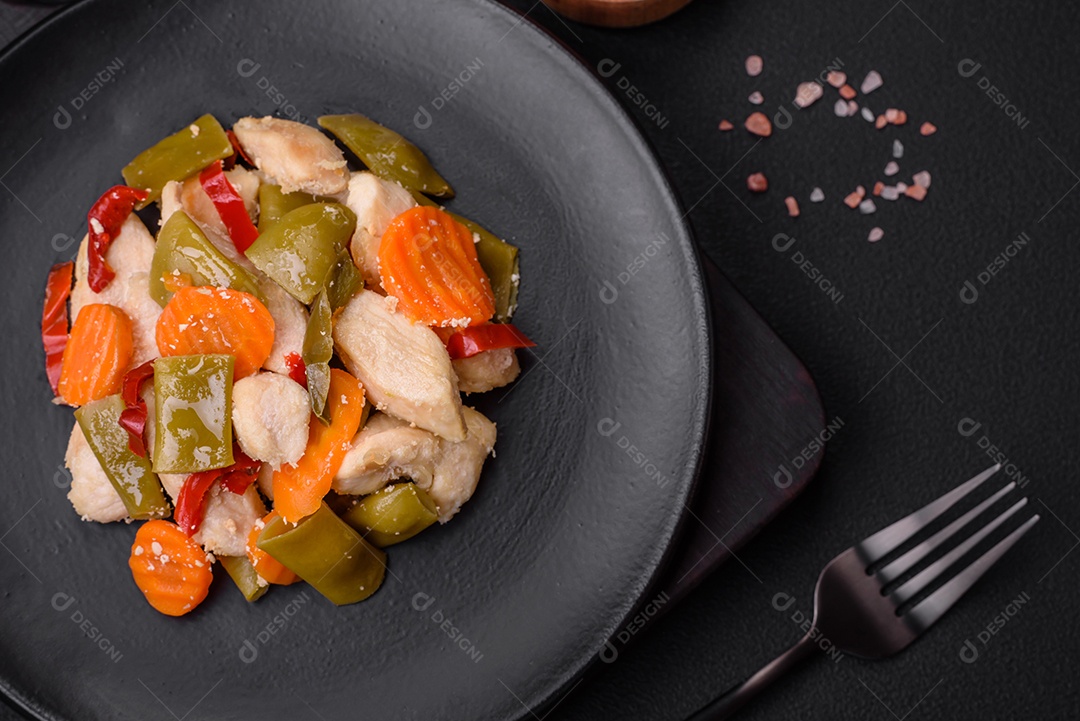 Deliciosas fatias de frango e legumes cozidos no vapor, cenouras, brócolis, espargos e pimentões em um fundo escuro de concreto