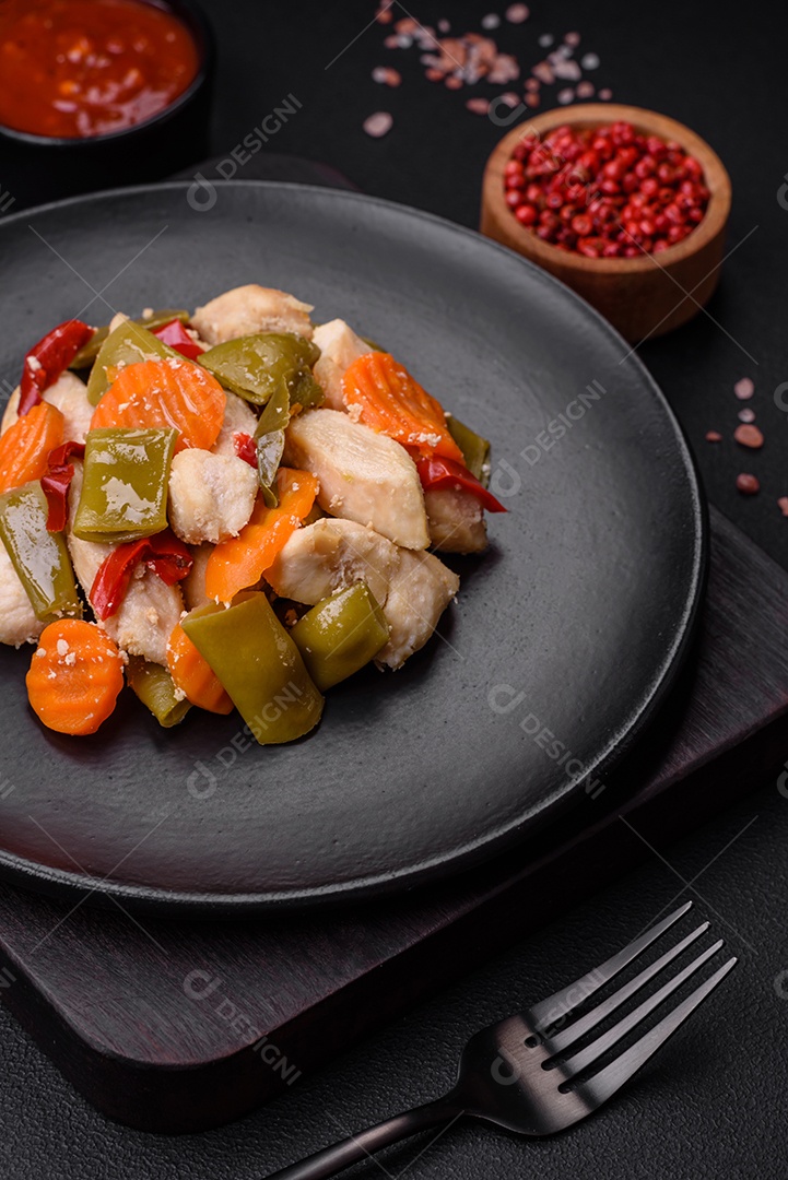 Deliciosas fatias de frango e legumes cozidos no vapor, cenouras, brócolis, espargos e pimentões em um fundo escuro de concreto