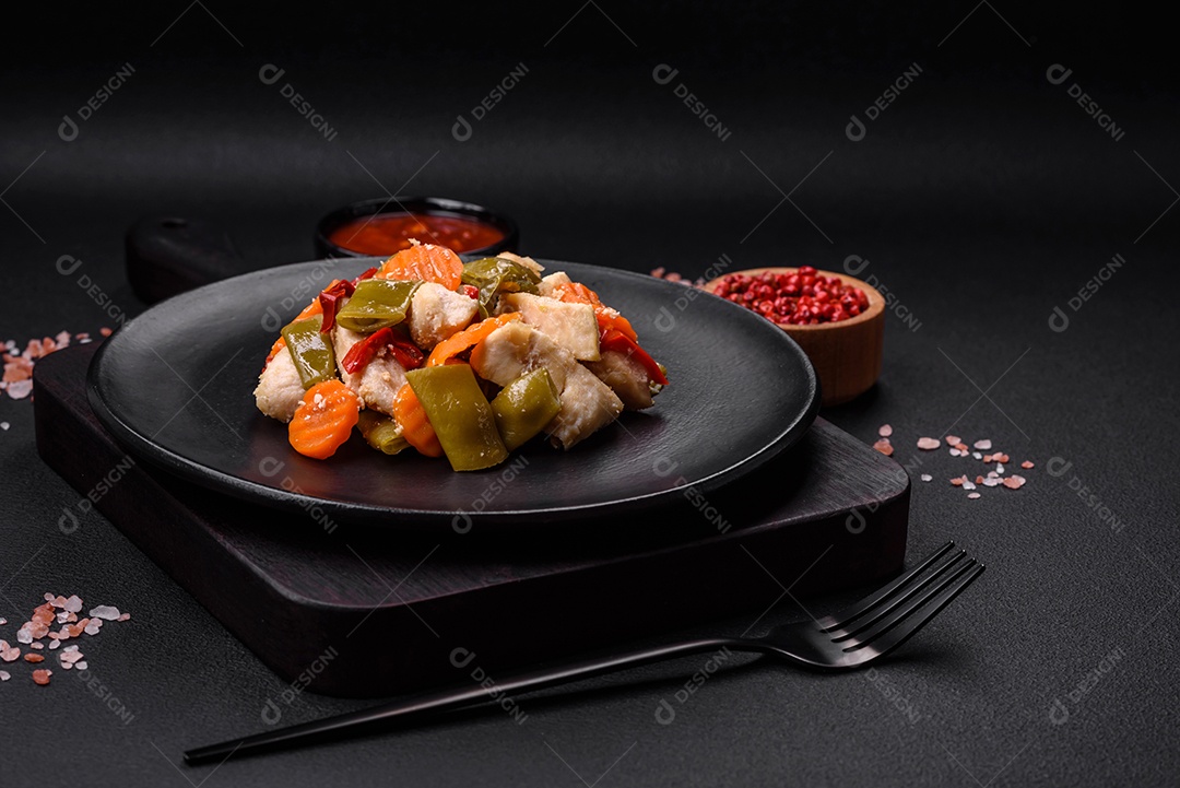 Deliciosas fatias de frango e legumes cozidos no vapor, cenouras, brócolis, espargos e pimentões em um fundo escuro de concreto