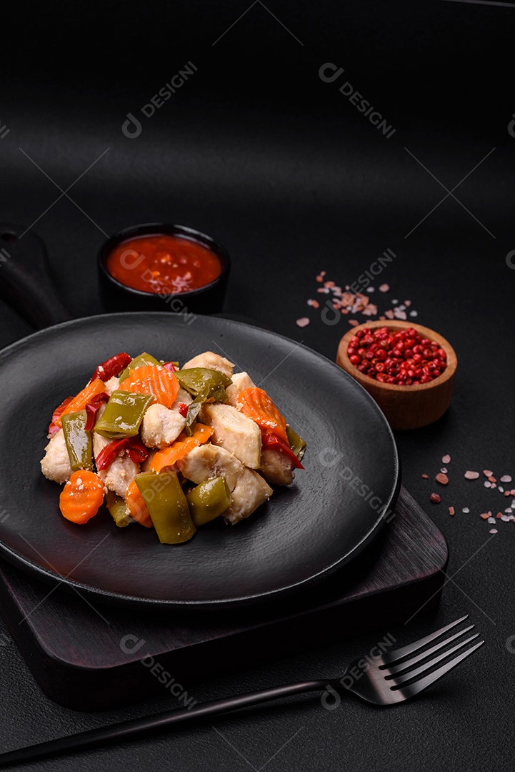 Deliciosas fatias de frango e legumes cozidos no vapor, cenouras, brócolis, espargos e pimentões em um fundo escuro de concreto