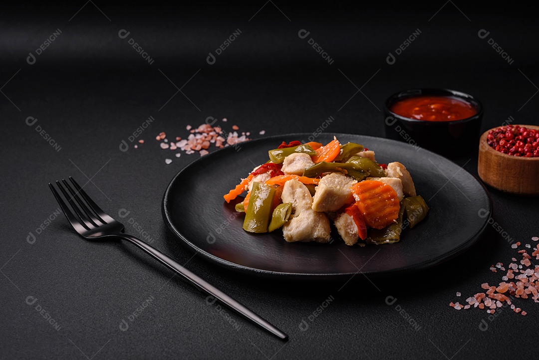 Deliciosas fatias de frango e legumes cozidos no vapor, cenouras, brócolis, espargos e pimentões em um fundo escuro de concreto