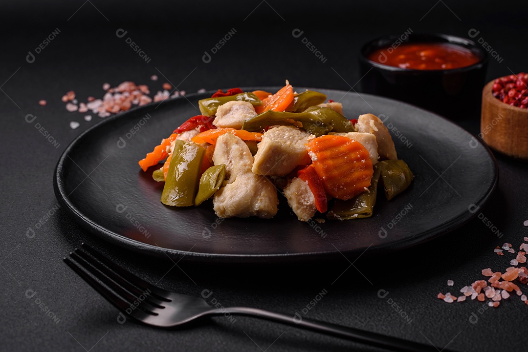 Deliciosas fatias de frango e legumes cozidos no vapor, cenouras, brócolis, espargos e pimentões em um fundo escuro de concreto