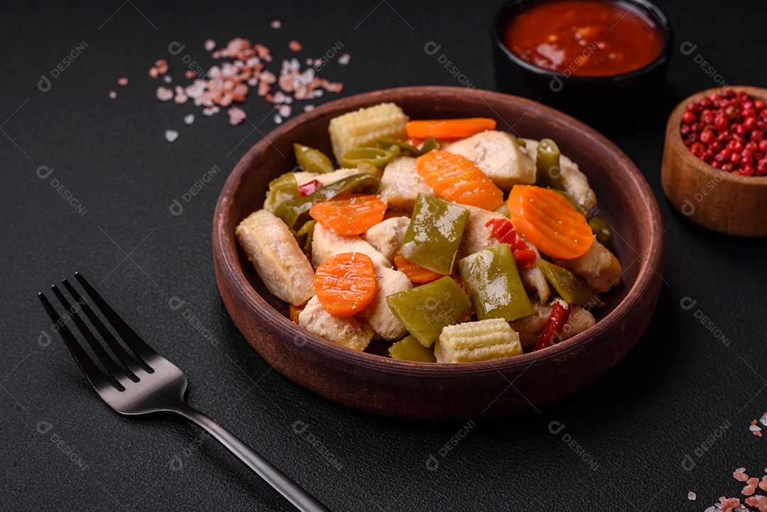 Deliciosas fatias de frango e legumes cozidos no vapor, cenouras, brócolis, espargos e pimentões em um fundo escuro de concreto