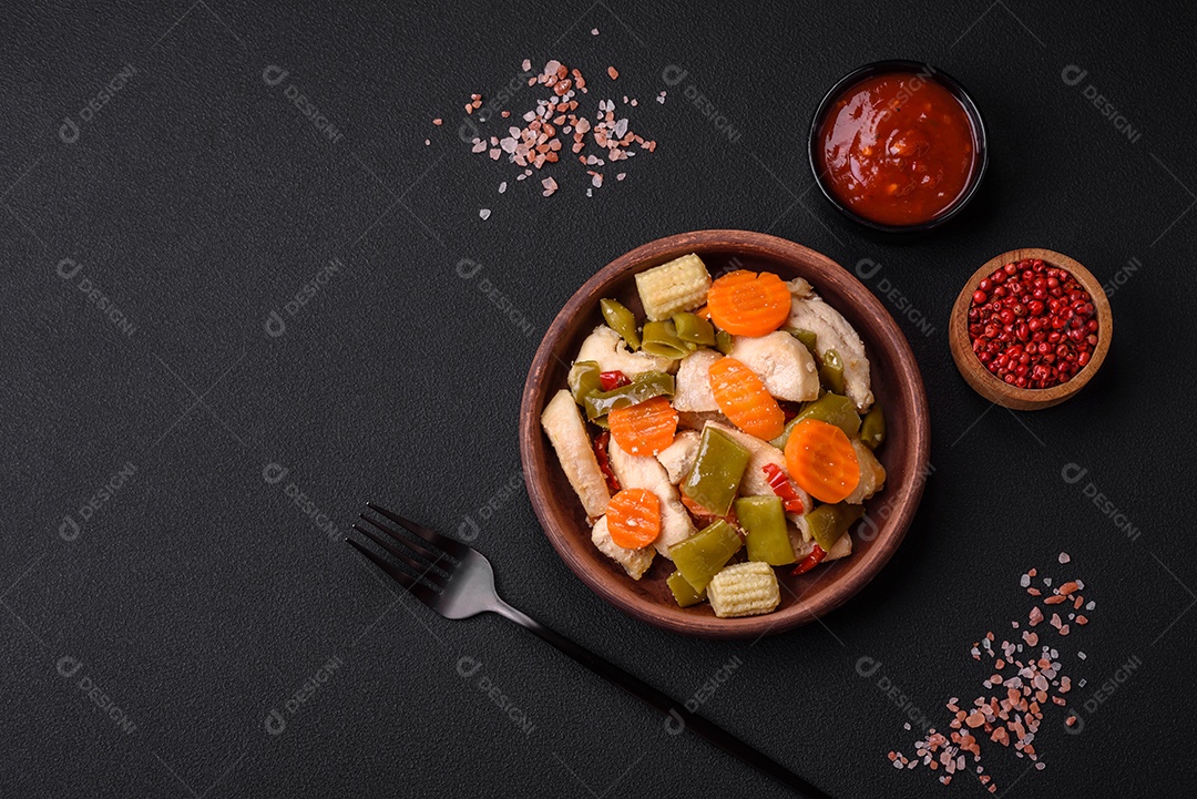 Deliciosas fatias de frango e legumes cozidos no vapor, cenouras, brócolis, espargos e pimentões em um fundo escuro de concreto