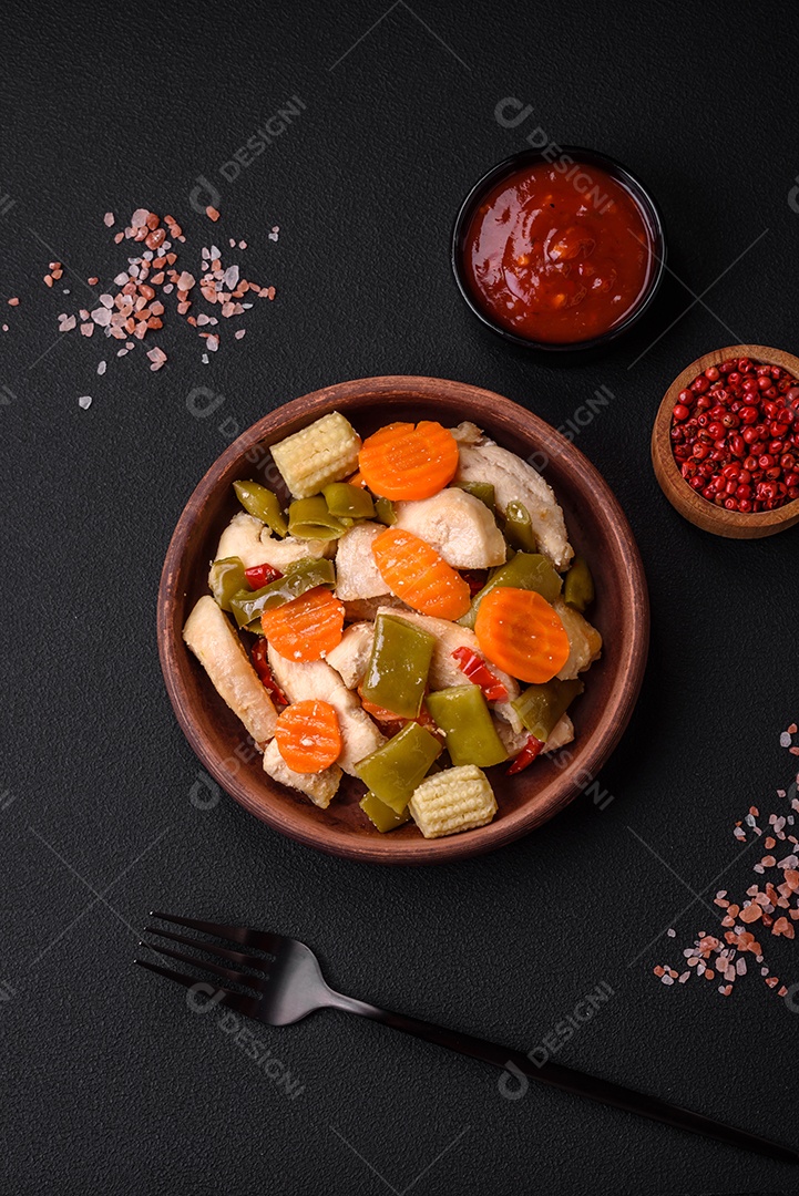 Deliciosas fatias de frango e legumes cozidos no vapor, cenouras, brócolis, espargos e pimentões em um fundo escuro de concreto