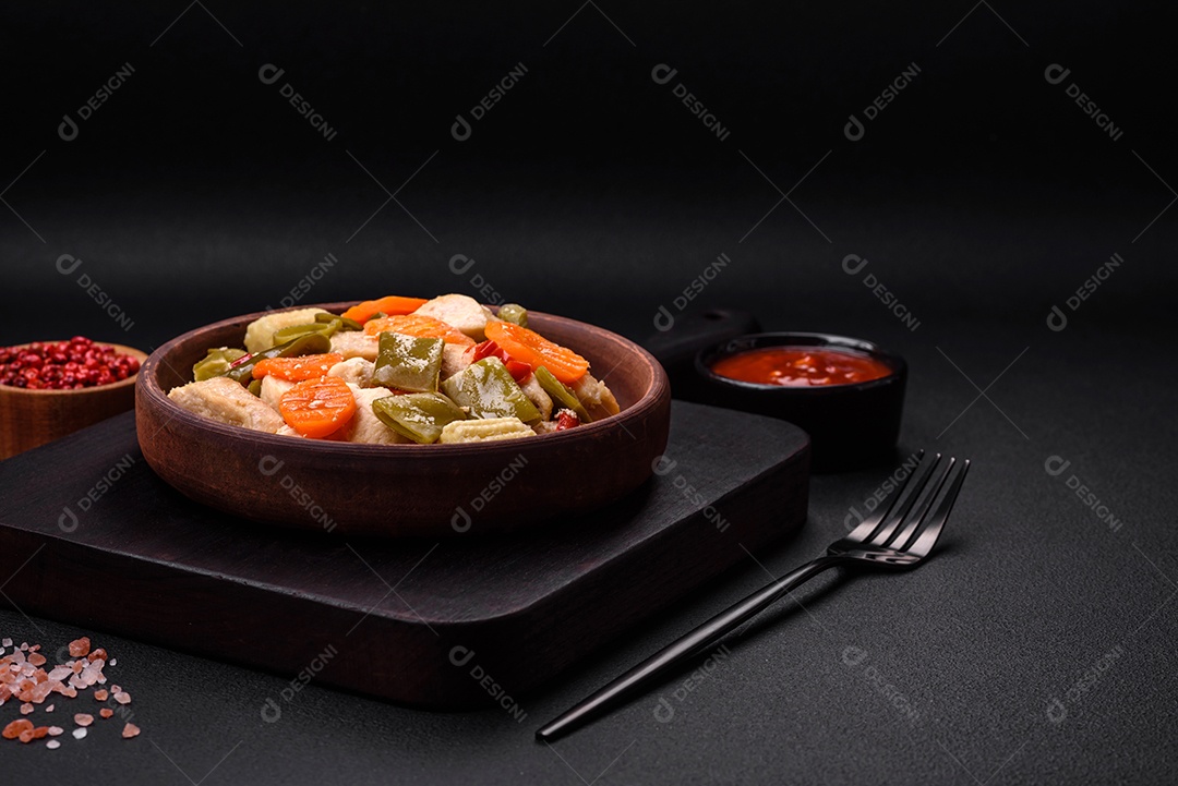 Deliciosas fatias de frango e legumes cozidos no vapor, cenouras, brócolis, espargos e pimentões em um fundo escuro de concreto