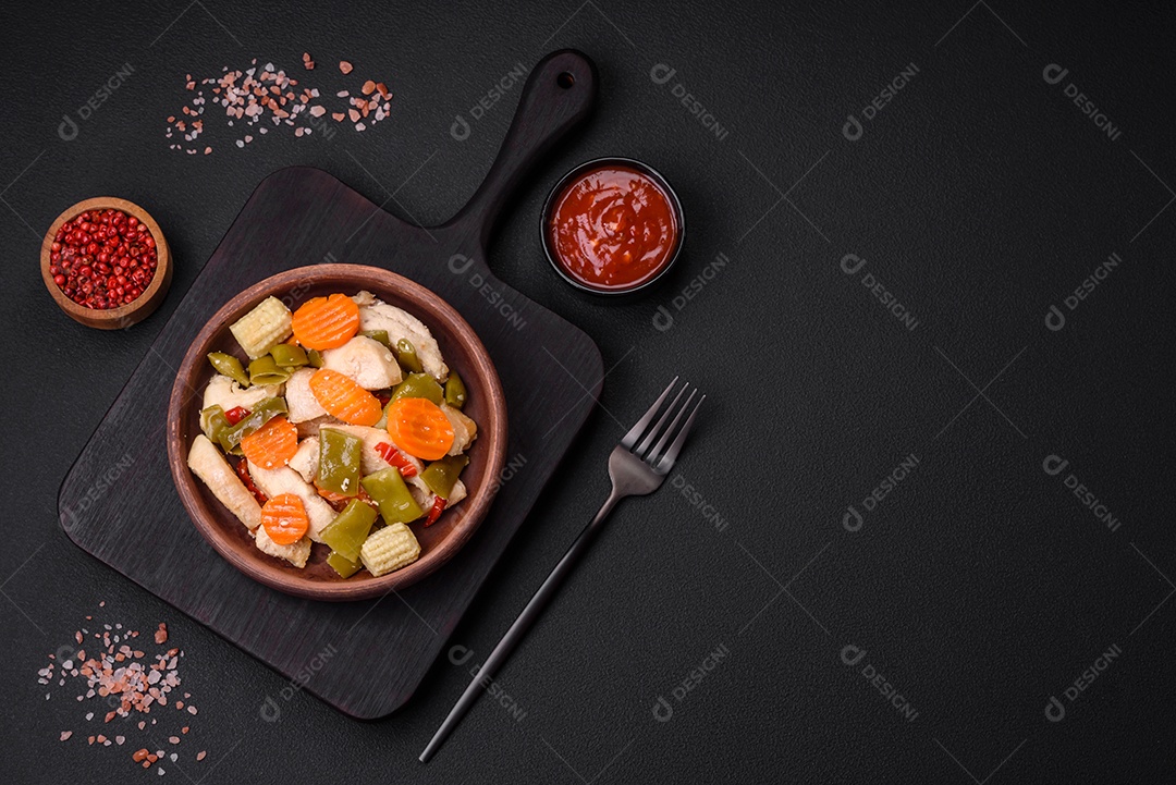 Deliciosas fatias de frango e legumes cozidos no vapor, cenouras, brócolis, espargos e pimentões em um fundo escuro de concreto