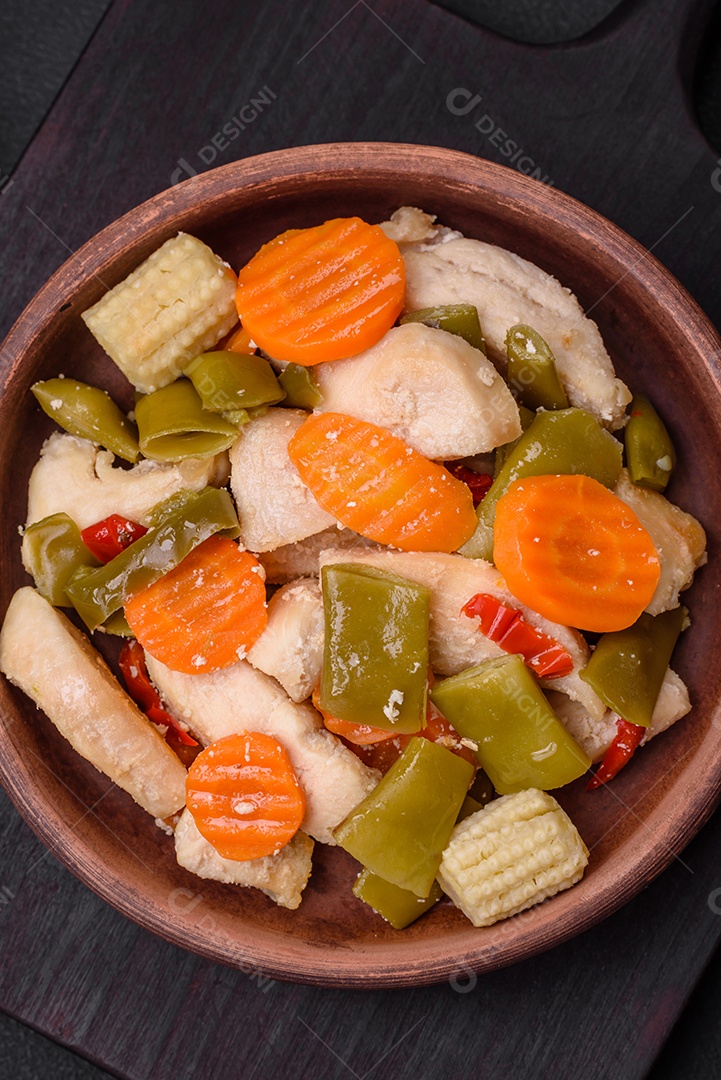 Deliciosas fatias de frango e legumes cozidos no vapor, cenouras, brócolis, espargos e pimentões em um fundo escuro de concreto