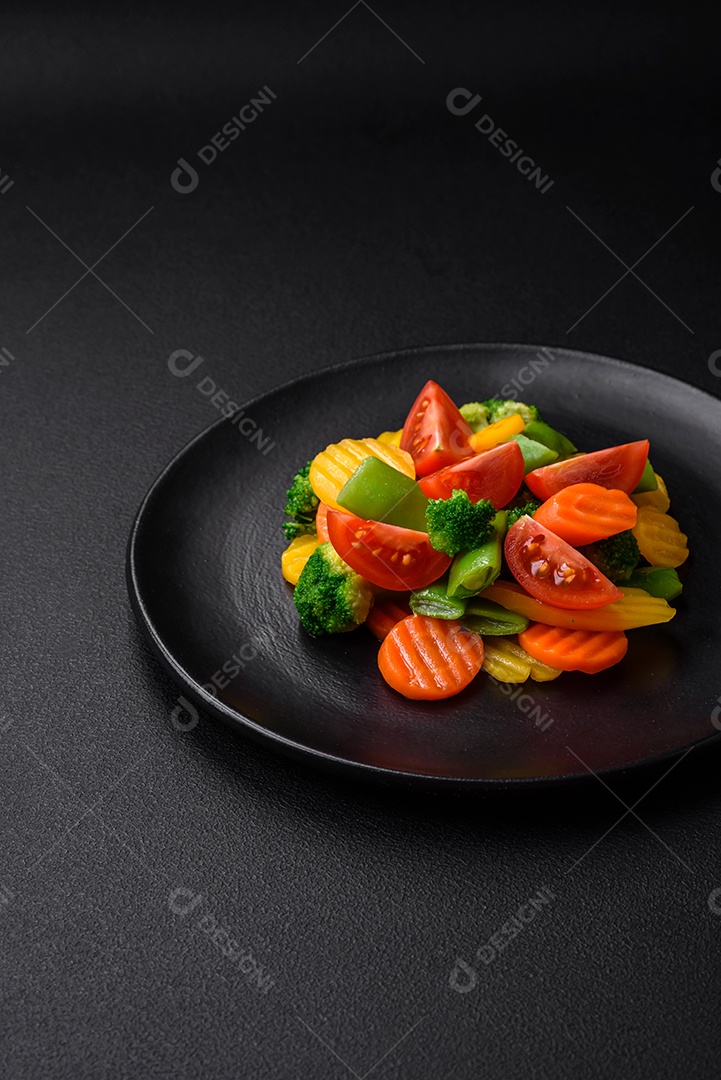 Salada de legumes frescos e cozidos no vapor, tomate cereja, brócolis, cenoura e feijão de espargos sobre um fundo escuro de concreto
