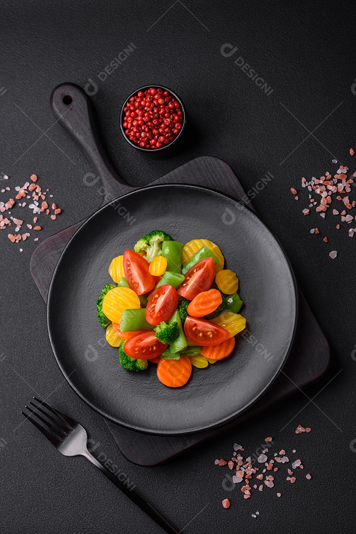 Salada de legumes frescos e cozidos no vapor, tomate cereja, brócolis, cenoura e feijão de espargos sobre um fundo escuro de concreto