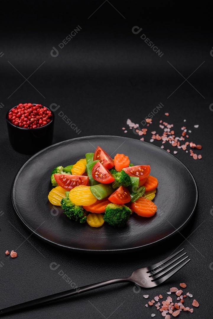 Salada de legumes frescos e cozidos no vapor, tomate cereja, brócolis, cenoura e feijão de espargos sobre um fundo escuro de concreto