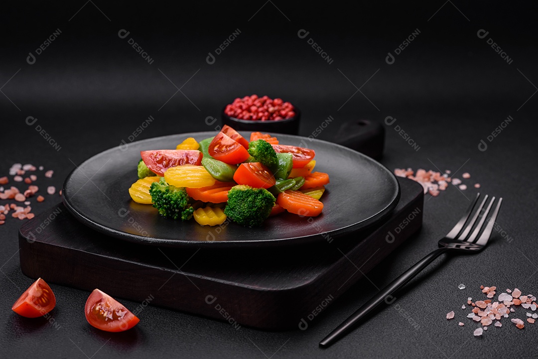 Salada de legumes frescos e cozidos no vapor, tomate cereja, brócolis, cenoura e feijão de espargos sobre um fundo escuro de concreto