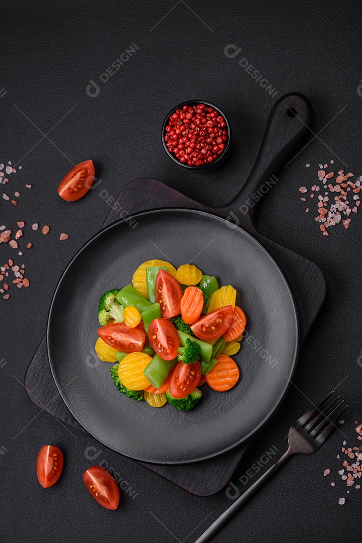 Salada de legumes frescos e cozidos no vapor, tomate cereja, brócolis, cenoura e feijão de espargos sobre um fundo escuro de concreto