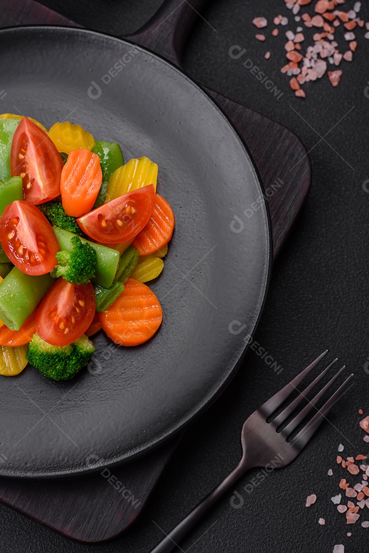 Salada de legumes frescos e cozidos no vapor, tomate cereja, brócolis, cenoura e feijão de espargos sobre um fundo escuro de concreto