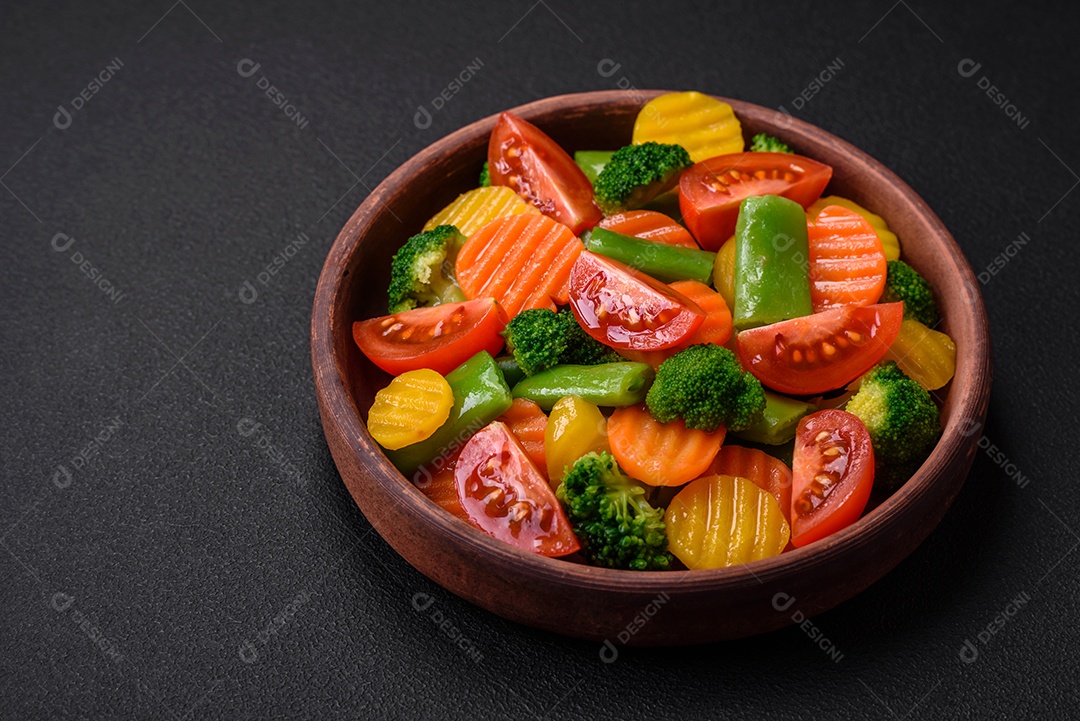 Salada de legumes frescos e cozidos no vapor, tomate cereja, brócolis, cenoura e feijão de espargos sobre um fundo escuro de concreto