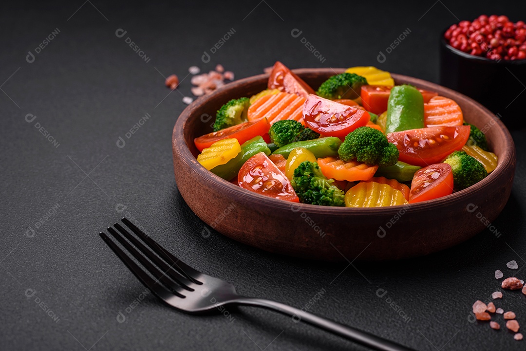 Salada de legumes frescos e cozidos no vapor, tomate cereja, brócolis, cenoura e feijão de espargos sobre um fundo escuro de concreto