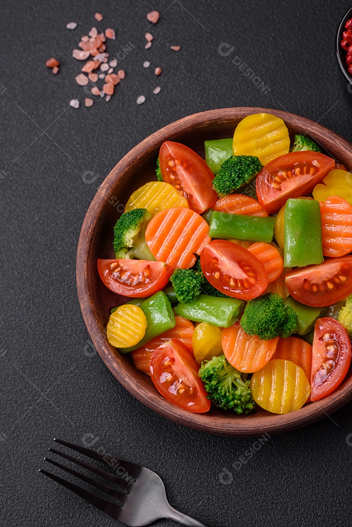 Salada de legumes frescos e cozidos no vapor, tomate cereja, brócolis, cenoura e feijão de espargos sobre um fundo escuro de concreto