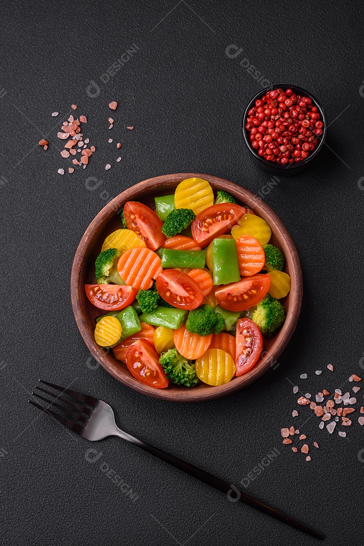 Salada de legumes frescos e cozidos no vapor, tomate cereja, brócolis, cenoura e feijão de espargos sobre um fundo escuro de concreto