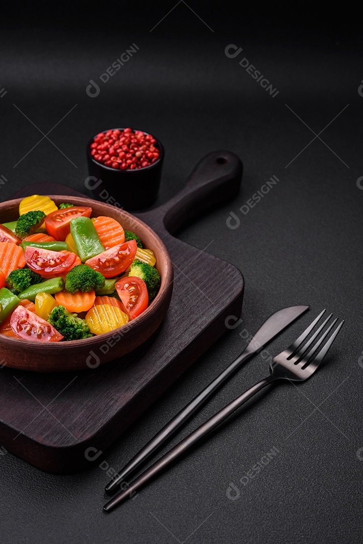 Salada de legumes frescos e cozidos no vapor, tomate cereja, brócolis, cenoura e feijão de espargos sobre um fundo escuro de concreto