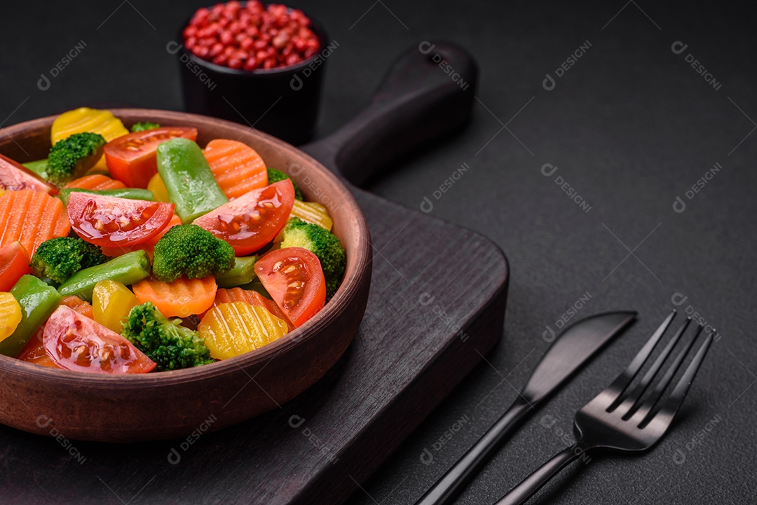 Salada de legumes frescos e cozidos no vapor, tomate cereja, brócolis, cenoura e feijão de espargos sobre um fundo escuro de concreto